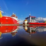 A large red ship next to a smaller red workboat